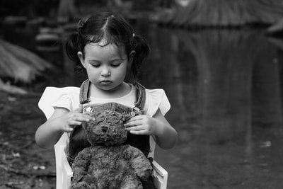 little girl looking at teddy bear by river
